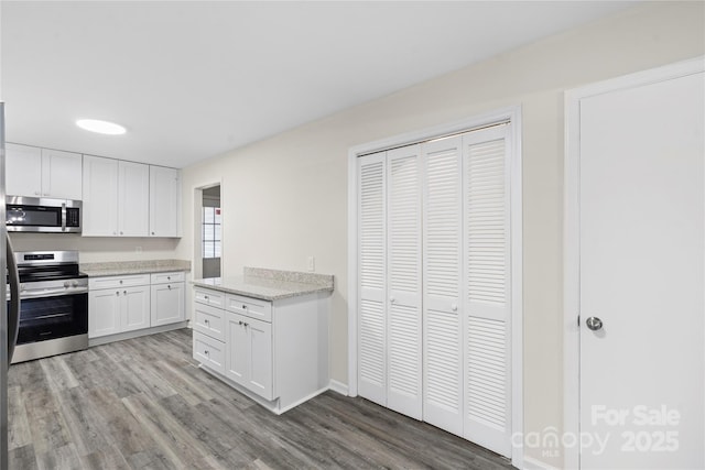 kitchen with white cabinets, stainless steel appliances, light stone counters, and light hardwood / wood-style flooring