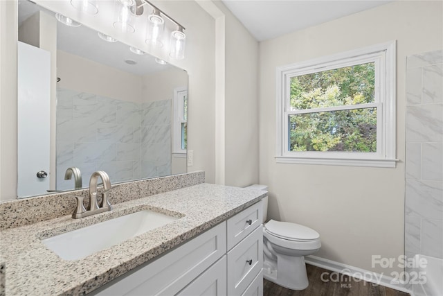 bathroom featuring a tile shower, vanity, wood-type flooring, and toilet