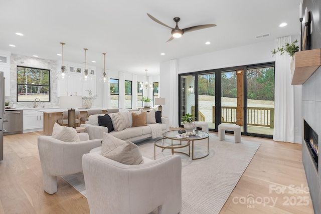 living room featuring french doors, sink, light hardwood / wood-style floors, a fireplace, and ceiling fan with notable chandelier