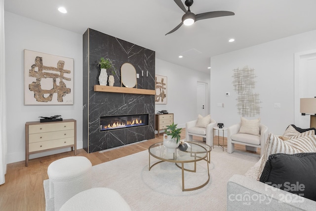 living room featuring ceiling fan, a fireplace, and light wood-type flooring