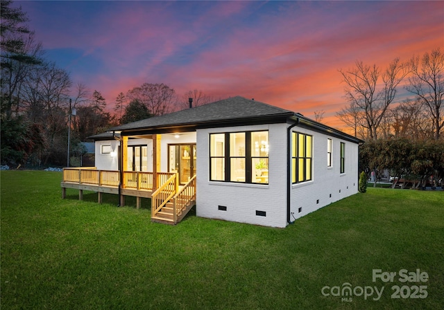 back house at dusk featuring a wooden deck and a yard