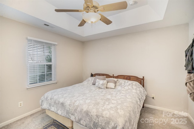 carpeted bedroom with a raised ceiling and ceiling fan