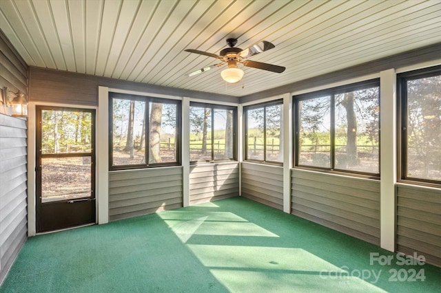 unfurnished sunroom featuring a healthy amount of sunlight, ceiling fan, and wooden ceiling