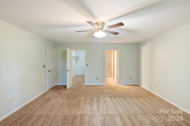 unfurnished bedroom with ceiling fan, a walk in closet, and light colored carpet