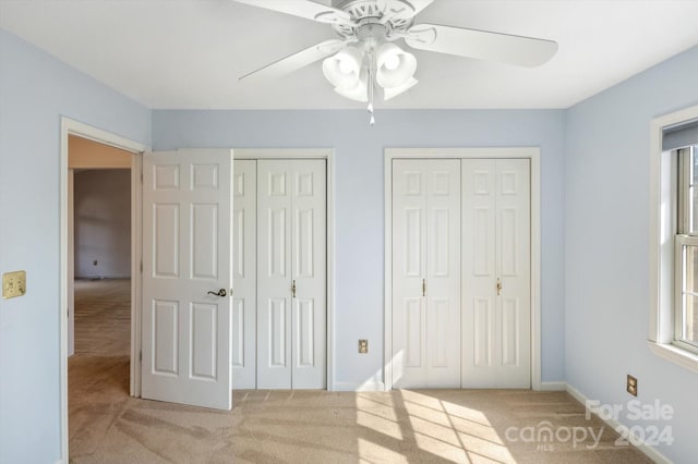 unfurnished bedroom featuring multiple closets, light carpet, and ceiling fan