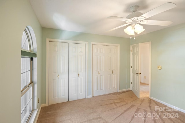 unfurnished bedroom featuring ceiling fan, multiple closets, and light colored carpet