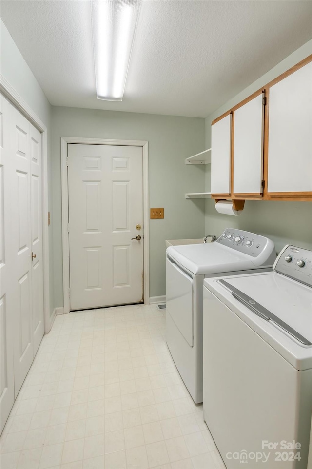 laundry room featuring a textured ceiling, washer and clothes dryer, and cabinets