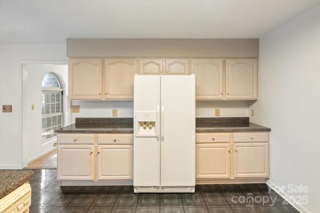 kitchen with light brown cabinetry, white appliances, dark countertops, and baseboards