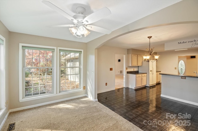 living area featuring arched walkways, ceiling fan with notable chandelier, visible vents, and baseboards