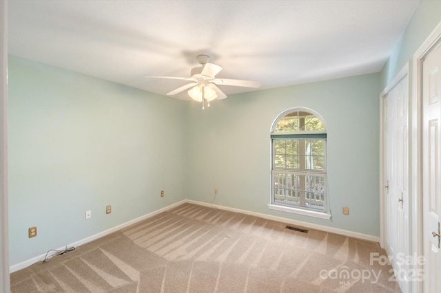 carpeted spare room with baseboards, visible vents, and a ceiling fan