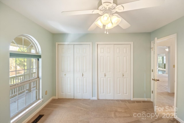 unfurnished bedroom featuring a ceiling fan, baseboards, visible vents, multiple closets, and carpet