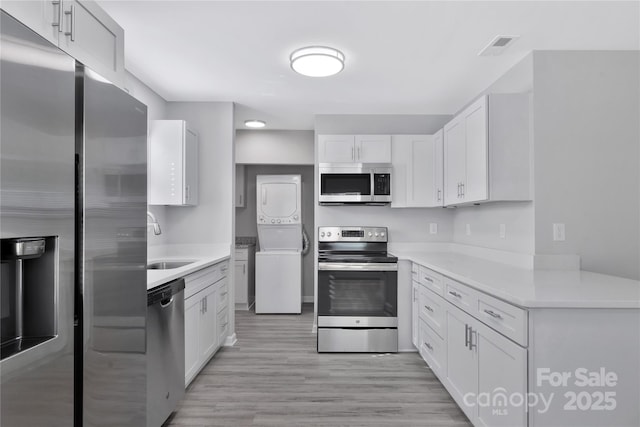 kitchen with white cabinets, stainless steel appliances, sink, and stacked washer and clothes dryer