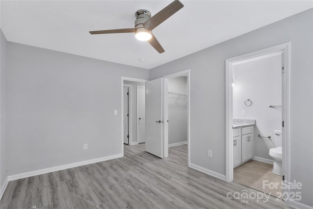 unfurnished bedroom featuring ensuite bathroom, a spacious closet, ceiling fan, light wood-type flooring, and a closet