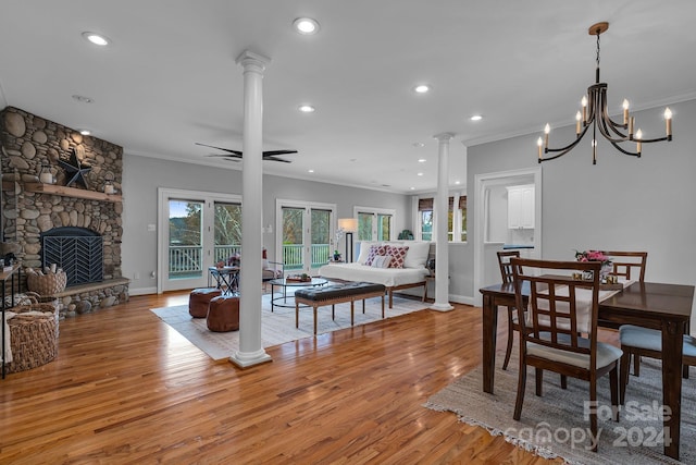 dining space with decorative columns, light hardwood / wood-style floors, a fireplace, ceiling fan with notable chandelier, and ornamental molding