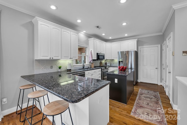 kitchen with appliances with stainless steel finishes, sink, white cabinets, a center island, and light hardwood / wood-style floors