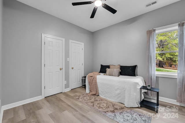 bedroom with ceiling fan, light hardwood / wood-style flooring, and two closets