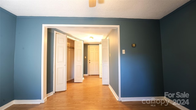 hallway with light hardwood / wood-style floors, crown molding, and a textured ceiling