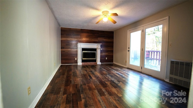 unfurnished living room featuring wooden walls, a textured ceiling, dark hardwood / wood-style floors, and a healthy amount of sunlight