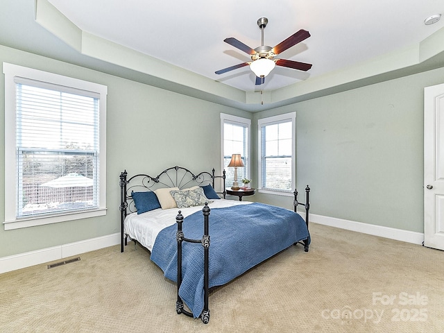 bedroom with ceiling fan, light colored carpet, and a tray ceiling