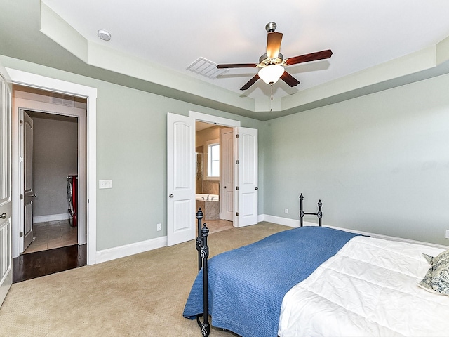 carpeted bedroom featuring ceiling fan, a raised ceiling, and connected bathroom