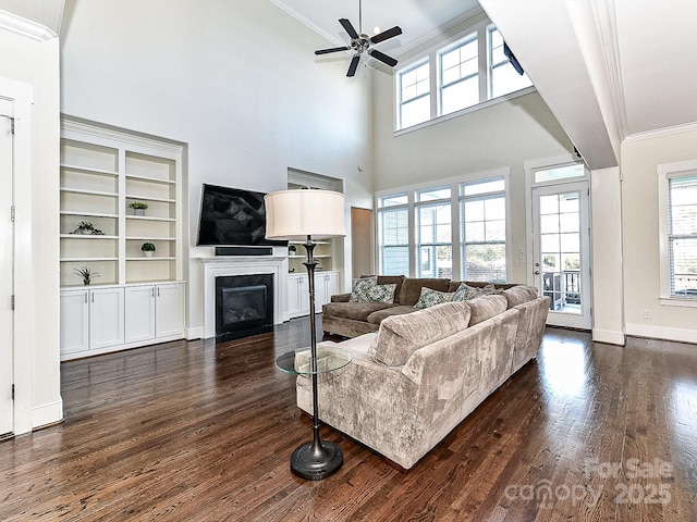 living room featuring dark wood-type flooring, ceiling fan, built in features, a towering ceiling, and ornamental molding