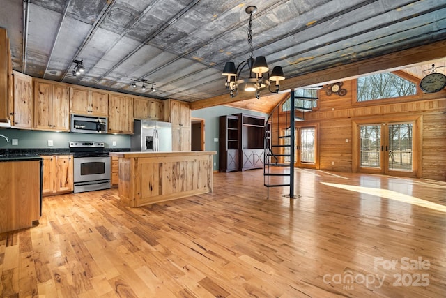 kitchen with stainless steel appliances, wooden walls, decorative light fixtures, and light hardwood / wood-style flooring