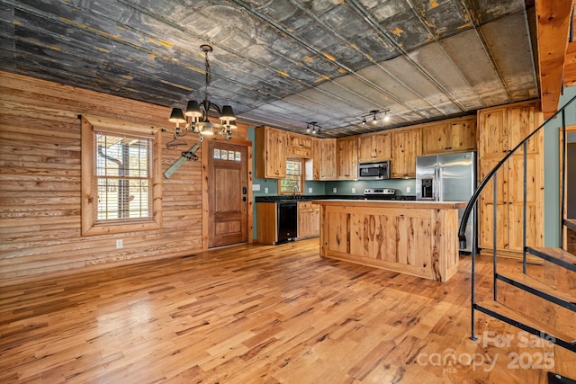 kitchen featuring stainless steel appliances, wooden walls, decorative light fixtures, and a notable chandelier