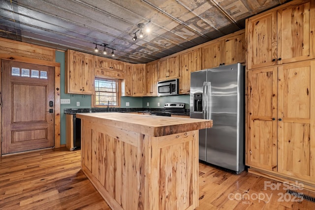 kitchen with appliances with stainless steel finishes, light wood-type flooring, a center island, and wood counters