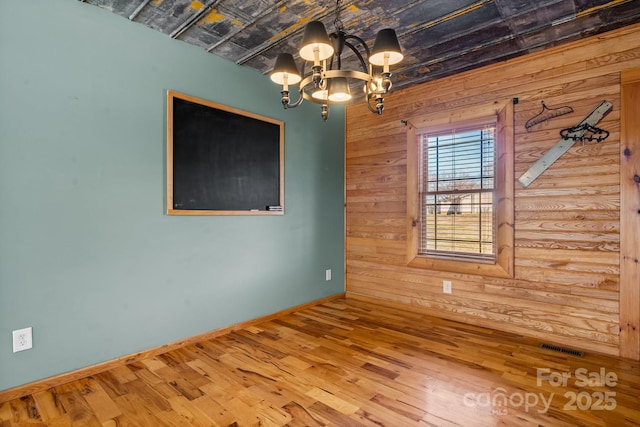 unfurnished room with hardwood / wood-style flooring, an inviting chandelier, and wooden walls