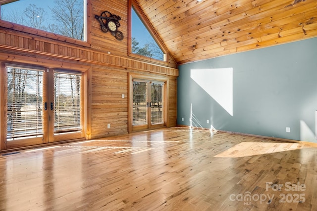 unfurnished living room featuring wooden ceiling, wooden walls, french doors, light wood-type flooring, and high vaulted ceiling