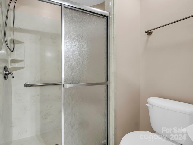 bathroom featuring toilet and a shower with shower door