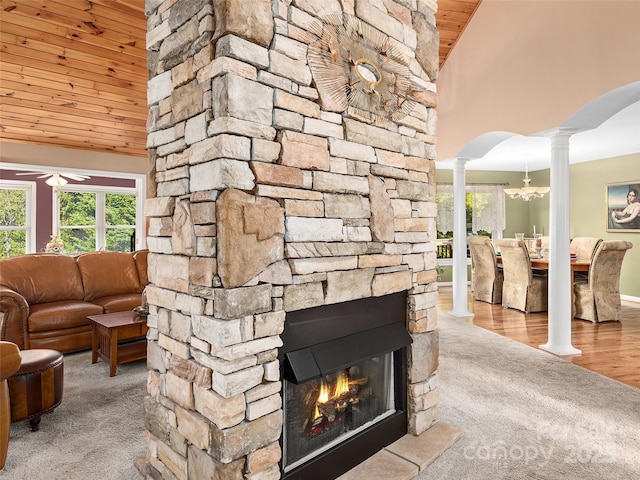 living room featuring decorative columns, light wood-type flooring, wood ceiling, a stone fireplace, and high vaulted ceiling