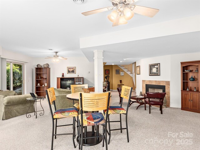 carpeted dining area featuring decorative columns, a tile fireplace, and ceiling fan