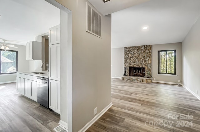 interior space with a stone fireplace, white cabinets, sink, stainless steel dishwasher, and light hardwood / wood-style flooring