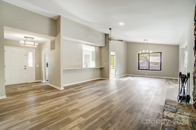 unfurnished living room featuring hardwood / wood-style flooring, ceiling fan with notable chandelier, and lofted ceiling