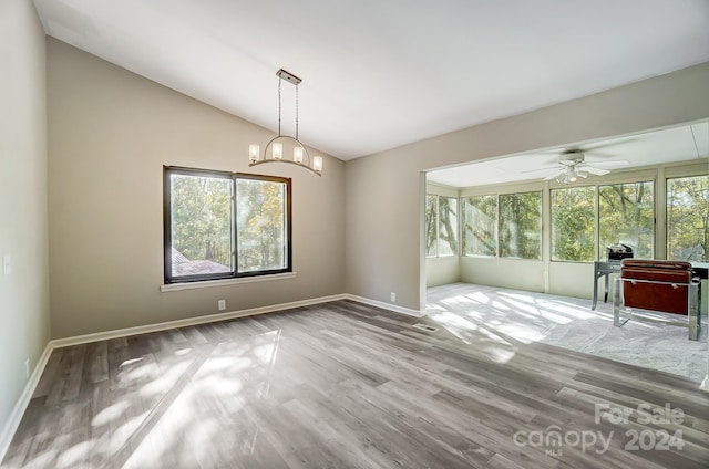 spare room with ceiling fan with notable chandelier, light hardwood / wood-style flooring, and lofted ceiling