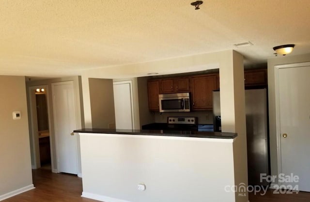 kitchen with appliances with stainless steel finishes, kitchen peninsula, a textured ceiling, and dark wood-type flooring