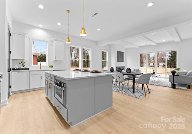 kitchen featuring pendant lighting, light wood-type flooring, beam ceiling, oven, and a center island