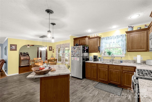 kitchen featuring stainless steel appliances, ornamental molding, a center island, decorative light fixtures, and light hardwood / wood-style floors