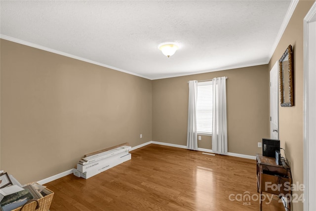 spare room featuring crown molding, wood-type flooring, and a textured ceiling