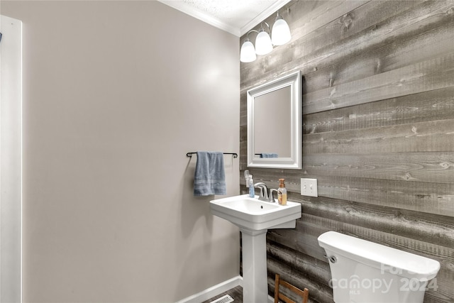 bathroom featuring toilet, wood walls, and crown molding