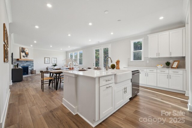 kitchen with dishwasher, white cabinetry, sink, ornamental molding, and a center island with sink