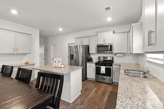 kitchen featuring light stone countertops, appliances with stainless steel finishes, dark hardwood / wood-style flooring, sink, and a breakfast bar area