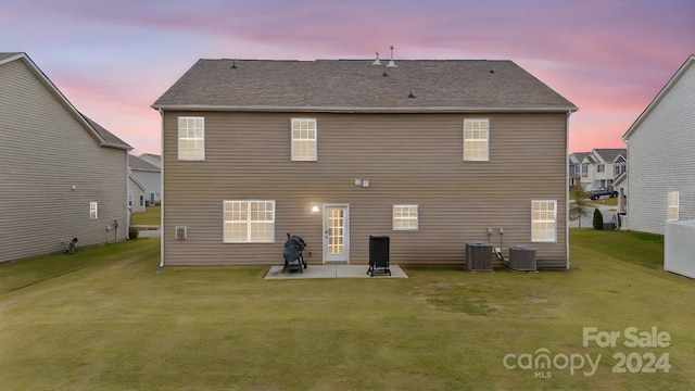 back house at dusk with a lawn, central AC unit, and a patio area