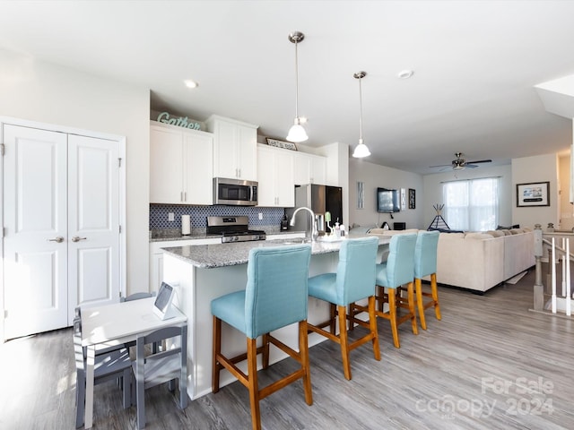 kitchen featuring appliances with stainless steel finishes, hanging light fixtures, white cabinets, light hardwood / wood-style flooring, and a kitchen island with sink