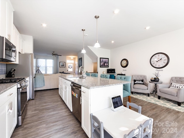 kitchen featuring hardwood / wood-style floors, an island with sink, white cabinetry, stainless steel appliances, and decorative light fixtures