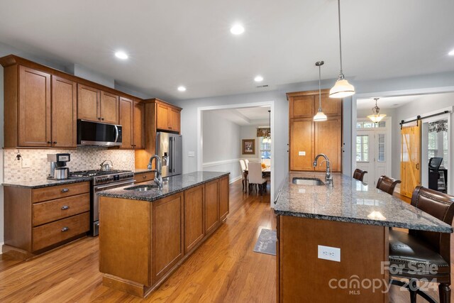 kitchen featuring a kitchen bar, light wood-type flooring, a barn door, hanging light fixtures, and stainless steel appliances