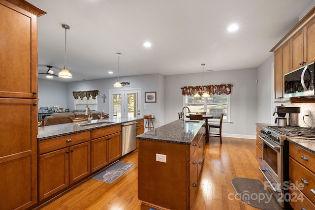 kitchen with a kitchen island with sink, stainless steel appliances, hanging light fixtures, and a wealth of natural light