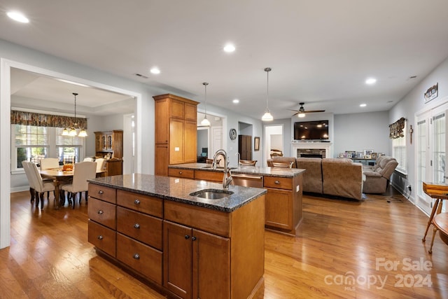 kitchen featuring a center island with sink, dark stone countertops, ceiling fan with notable chandelier, light hardwood / wood-style floors, and decorative light fixtures