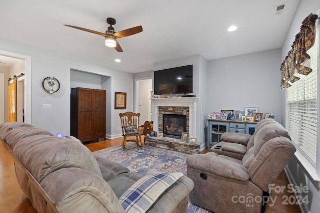 living room with ceiling fan, a stone fireplace, and light hardwood / wood-style flooring